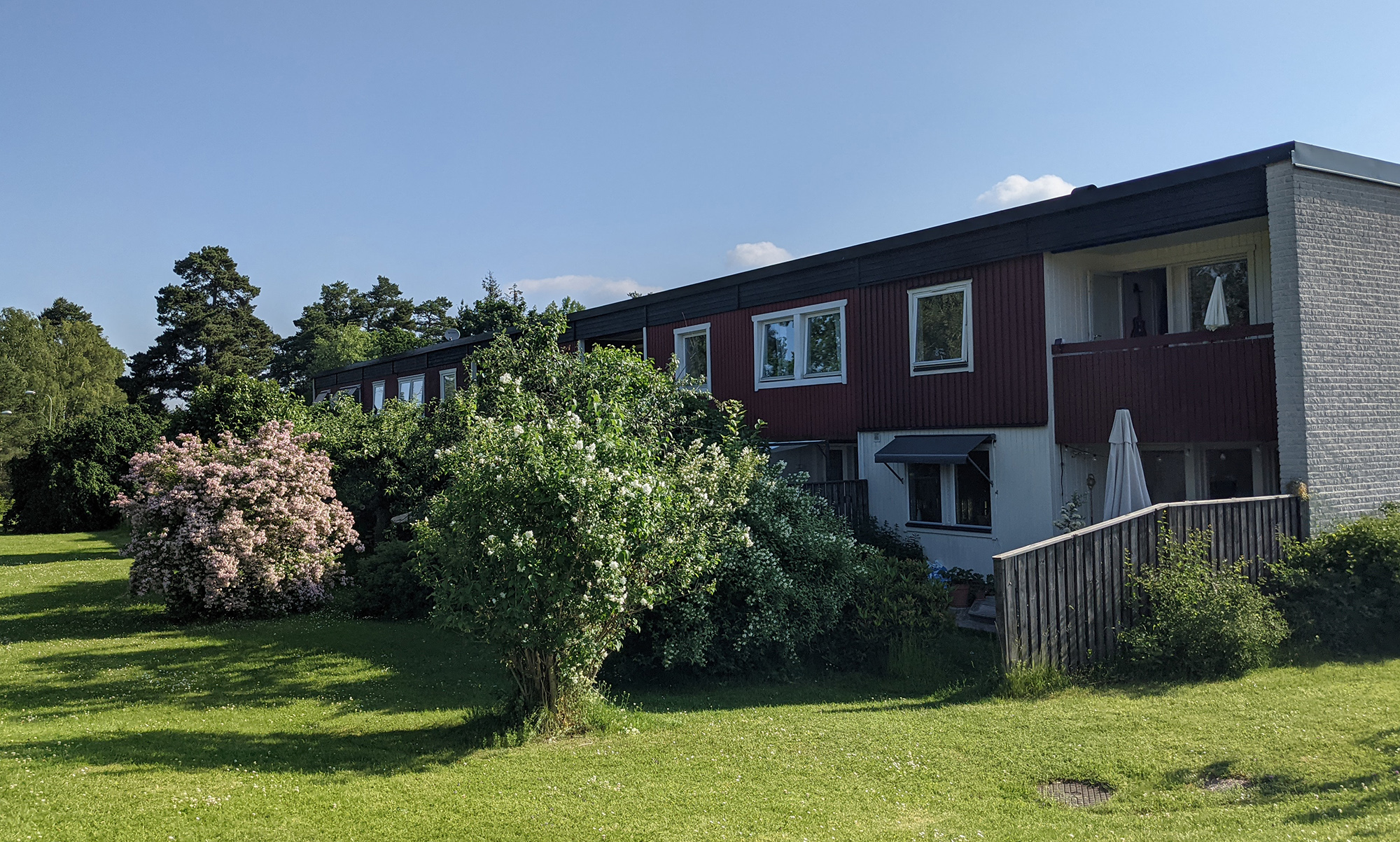 Rött radhus med trädgård och blommande buskar en solig sommardag
